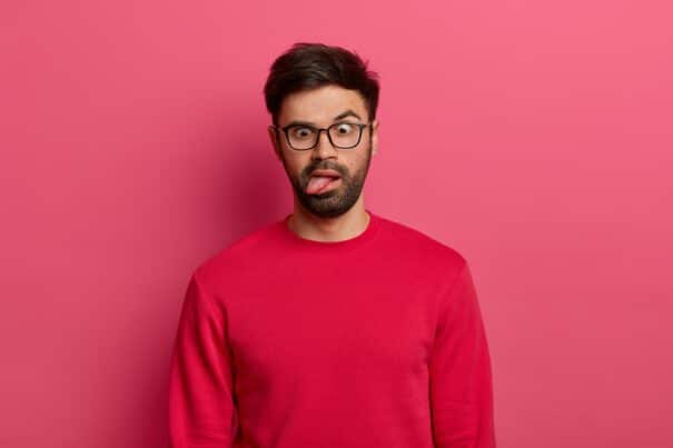 - photo crazy bearded man sticks out tongue crosses eyes feels tired bored wears glasses red sweater foolishes around poses against pink wall comic face expressions concept - ภาพที่ 3