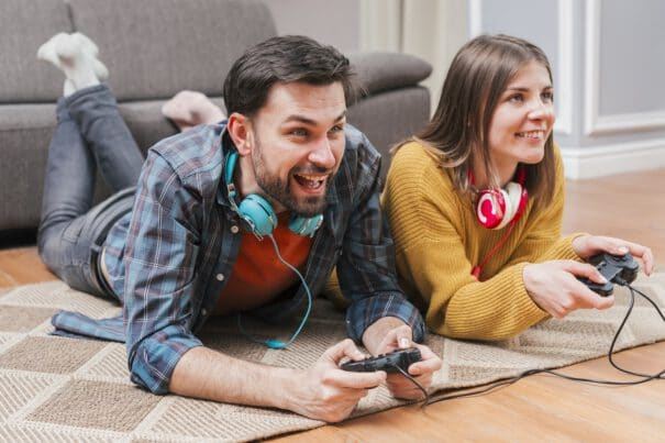 แฟนติดเกมจนไม่สนใจ ทำไงดี - smiling young couple lying floor playing video game with joystick home - ภาพที่ 7