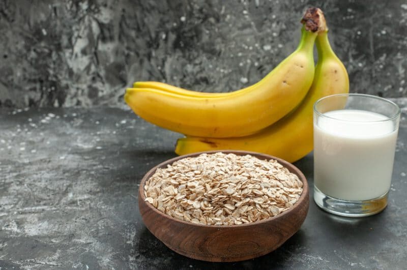 - front close view breakfast background with organic oat bran brown wooden pot milk glass bananas bundle dark background - ภาพที่ 7