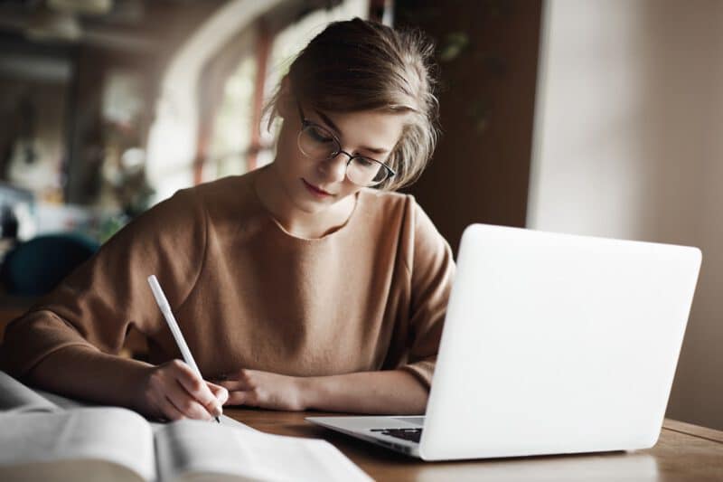 เขียนนิยาย - hardworking focused woman trendy glasses concentrating writing essay sitting cozy cafe near laptop working making notes carefully - ภาพที่ 7