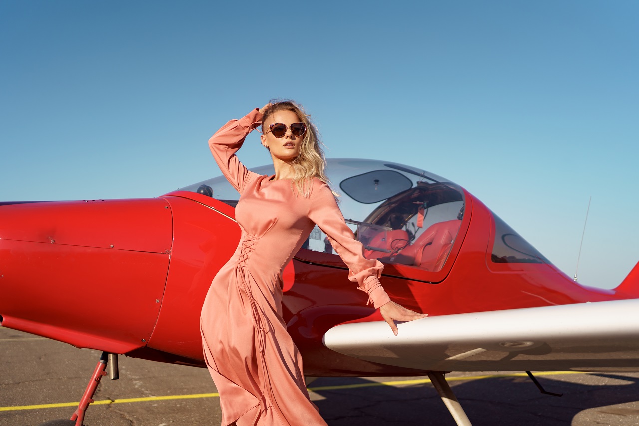 ถ่ายรูปบนเครื่องบิน - pretty blond woman with wavy hair wearing pink silk classy dress posing near private plane - ภาพที่ 1