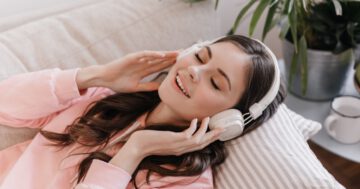 อาการเพลงติดหู - young woman puts her massive headphones relaxes sofa cozy apartment Large - ภาพที่ 1